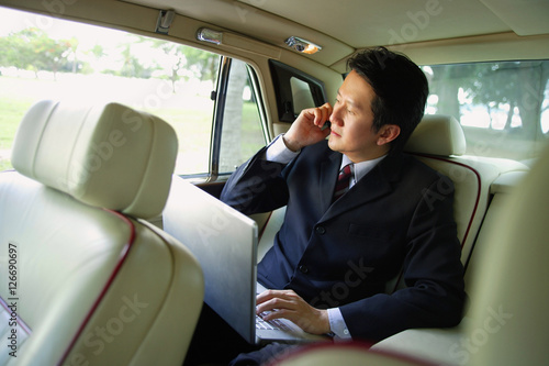 Businessman in car, using laptop and mobile phone