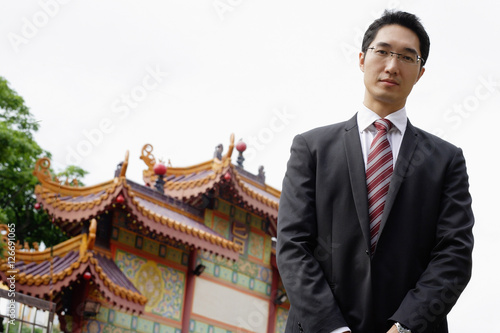 Businessman standing, looking at camera, Chinese temple gates in background