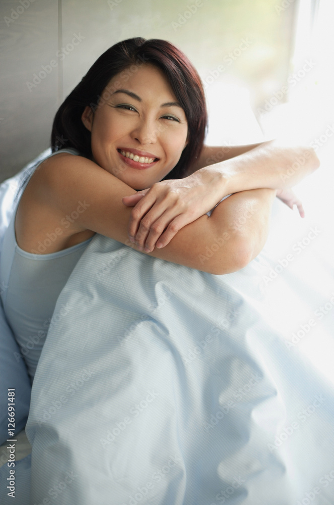 Woman on bed hugging knees, arms crossed Woman on bed hugging knees, arms crossed