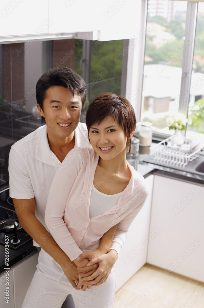 Couple embracing in kitchen, smiling at camera Couple embracing in kitchen, smiling at camera