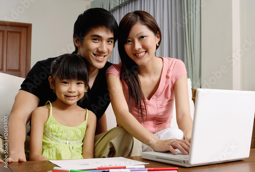 Family with one daughter, looking at camera, mother using laptop