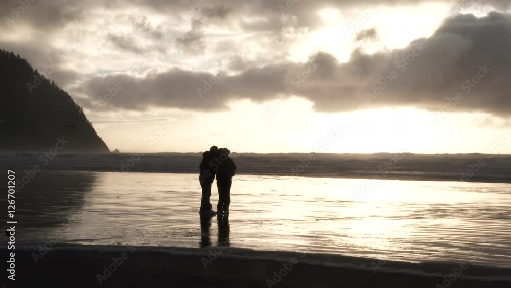 Unrecognizable silhouetted couple taking photo together with two birds flying by at the Pacific Ocean in Oregon during sunset. Unrecognizable silhouetted couple taking photo together with two birds flying by at the Pacific Ocean in Oregon during sunset.