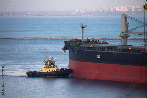 Obraz na plátně ship berthing at port with tug assistance on mooring rope with city on backgroun