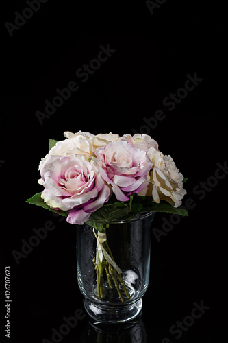 Ramo de rosas en florero de cristal sobre fondo negro.