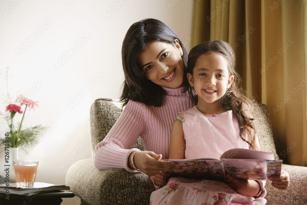 little girl sits on mother's lap, both smile at camera