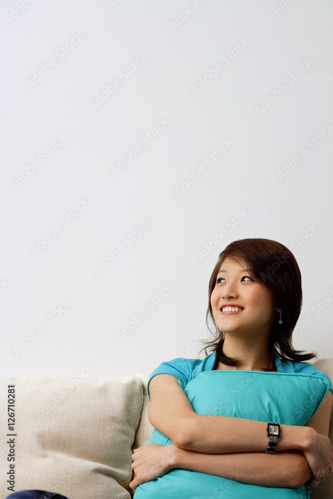 Woman sitting on sofa, hugging cushion, looking away Woman sitting on sofa, hugging cushion, looking away
