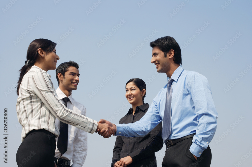 four business colleagues, two shaking hands