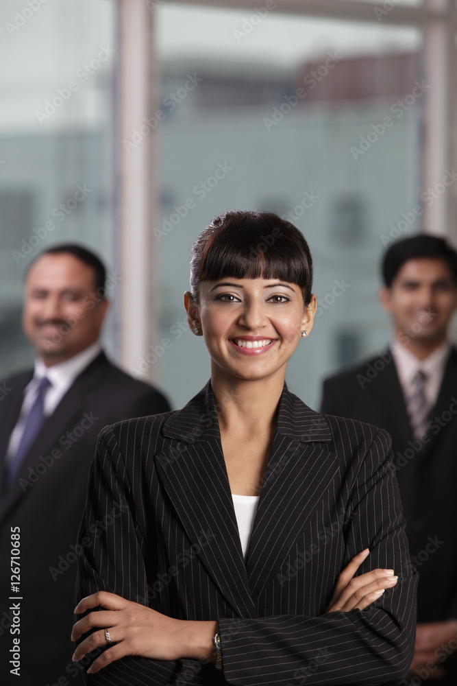 Indian woman smiling with arms folded in front of two colleagues Indian woman smiling with arms folded in front of two colleagues
