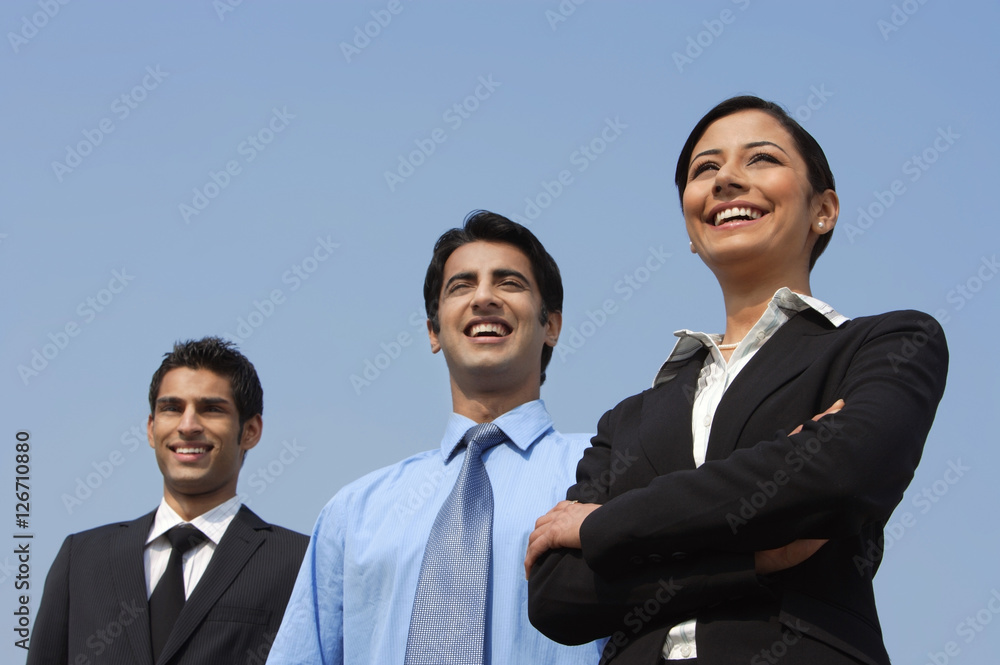 three colleagues standing, woman has arms folded three colleagues standing, woman has arms folded