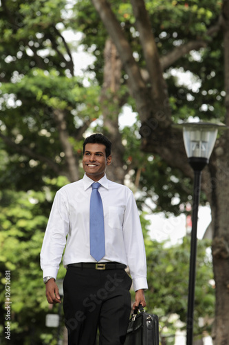 Indian man walking outside holding briefcase and smiling