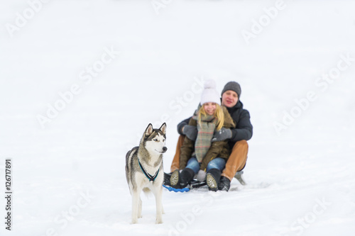 Happy couple sledding with toboggan and dog in winter