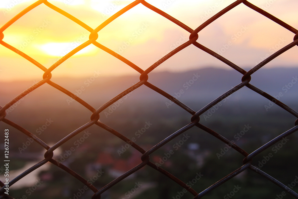 Mesh fence close-up on a blurred background of Beautiful scenery during time the sunset. The nature and the freedom concept Mesh fence close-up on a blurred background of Beautiful scenery during time the sunset. The nature and the freedom concept