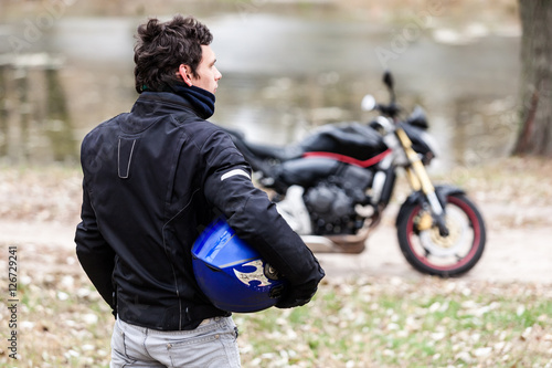 Biker standing near motorcycle holding his blue helmet.