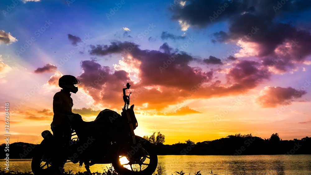 Naklejka premium Silhouette biker with his motorbike beside the natural lake and beautiful twilight sky.
