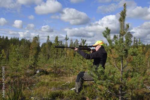 Quadro em tela Young female moose hunter sitting on a stump aiming with her rifle with silencer ,picture from the North of Sweden