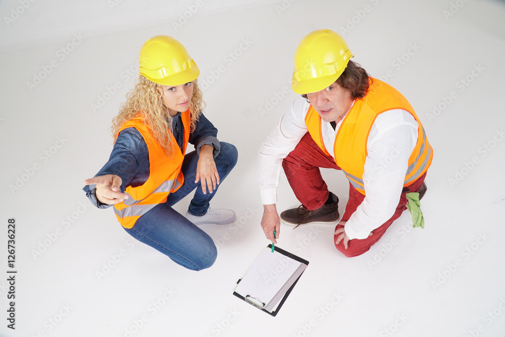 Two crouched construction workers, a man and a blonde girl, on white background. View from above Two crouched construction workers, a man and a blonde girl, on white background. View from above