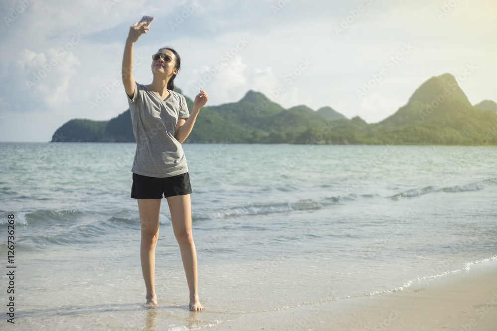 portrait of young asian woman using smart phone at beach.technology concept.blurred beach sea background.light effect added.take a selfy portrait of young asian woman using smart phone at beach.technology concept.blurred beach sea background.light effect added.take a selfy