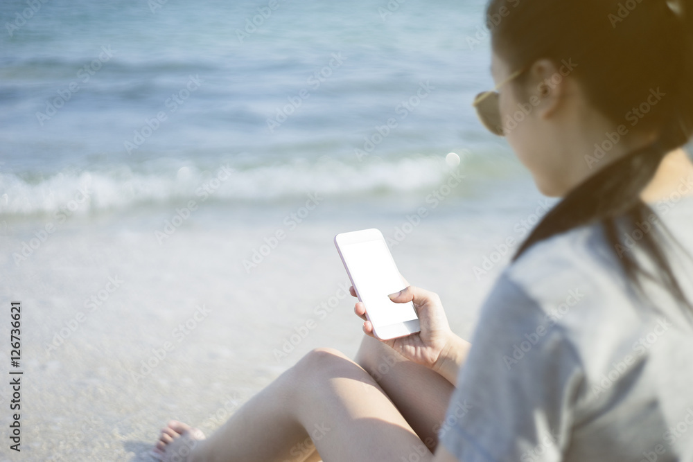 portrait of young asian happy woman using smart phone at beach.technology concept.blurred beach sea background.clipping path included.light effect added.