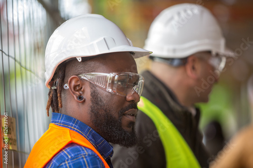 Profile close up of two engineers wearing protective hardhats. Selective focus