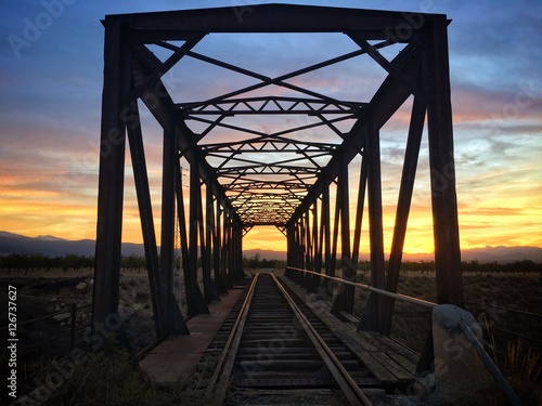 Puesta de sol vista a través de un puente metálico de tren