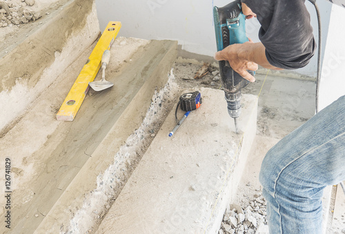 Partial focus of a man is working with reinforce concrete stair structure modification using hand drill machine in construction site
