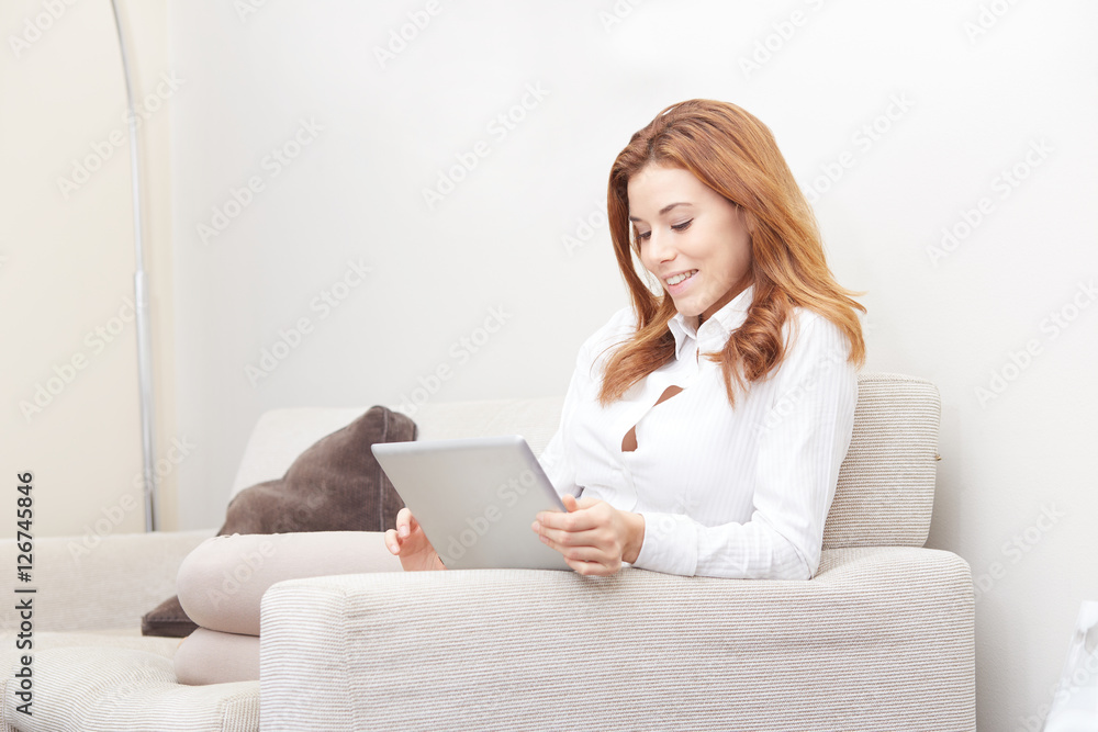 Smiling happy woman sitting on the sofa and using tablet pc Smiling happy woman sitting on the sofa and using tablet pc