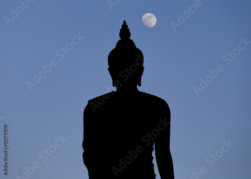 Fotografie A moon shines in a sky over a large silhouetted Buddha statue in Bangkok, Thailand