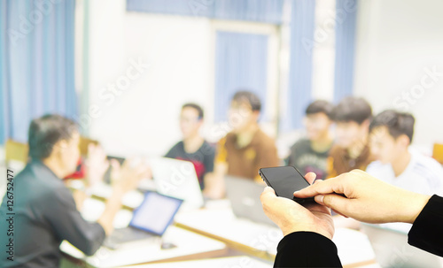 Businessman is using mobile phone over blurred people during training in a room