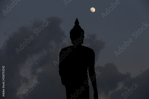 Fotografie A moon shines in a sky over a large silhouetted Buddha statue in Bangkok, Thailand