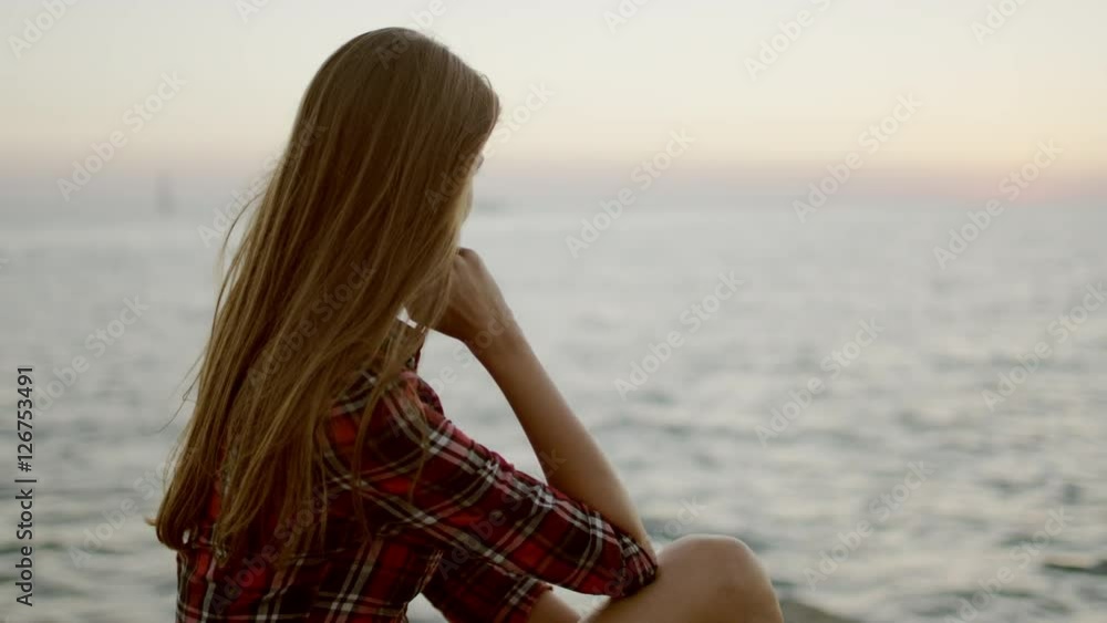 view of a young girl sitting down by sea shore looking at the horizon view of a young girl sitting down by sea shore looking at the horizon