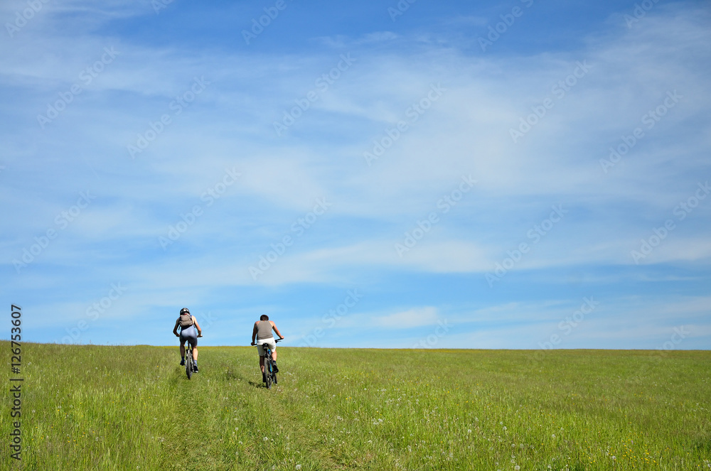 Two bikers silhouette on the trip in nature with evergreen trees and meadow. Bikers are moving on horizon which is colorful and full of last sunset light Two bikers silhouette on the trip in nature with evergreen trees and meadow. Bikers are moving on horizon which is colorful and full of last sunset light