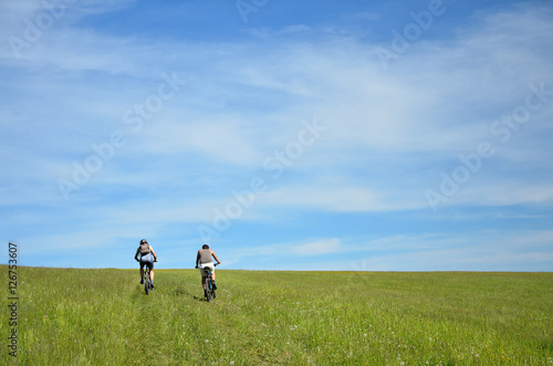 Two bikers silhouette on the trip in nature with evergreen trees and meadow. Bikers are moving on horizon which is colorful and full of last sunset light