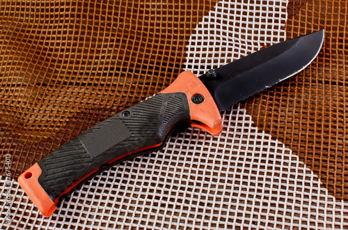 Orange folding knife with an iron grip well on Military Camoufla photo