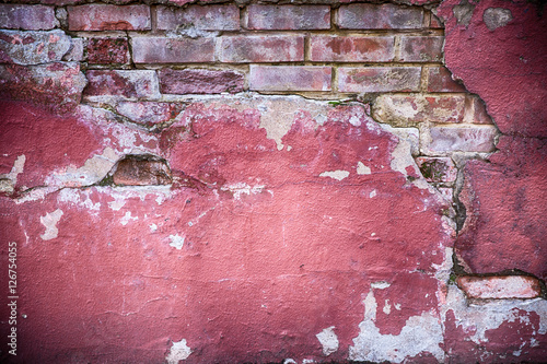 Decaying wall grunge texture. Red paint and exposed brick with plaster falling off photo