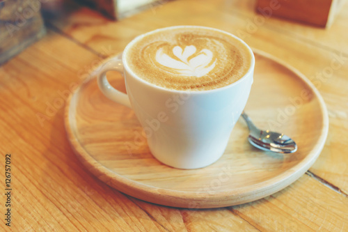 cup of coffee with heart pattern in a white cup on wooden backgr