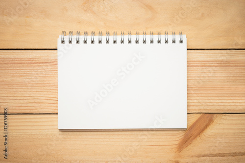 Blank notebook page in the middle of wood office desk table. Top view, flat lay.