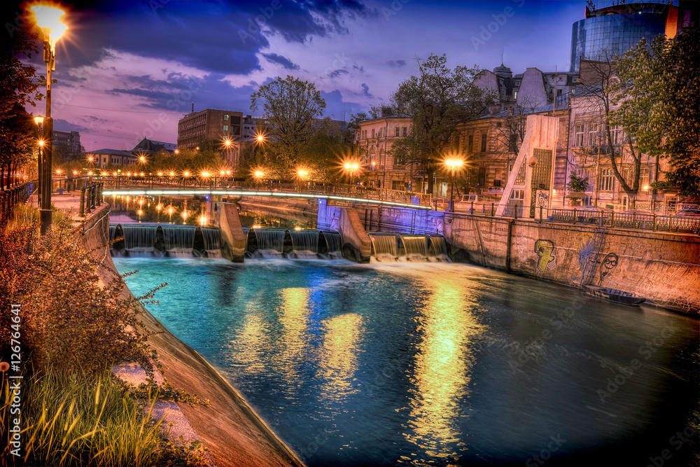 The Dambovita river in Bucharest, Romania. Photo taken at dusk with turquoise reflections in the water. Also city lights and a luminated bridge in the middle.