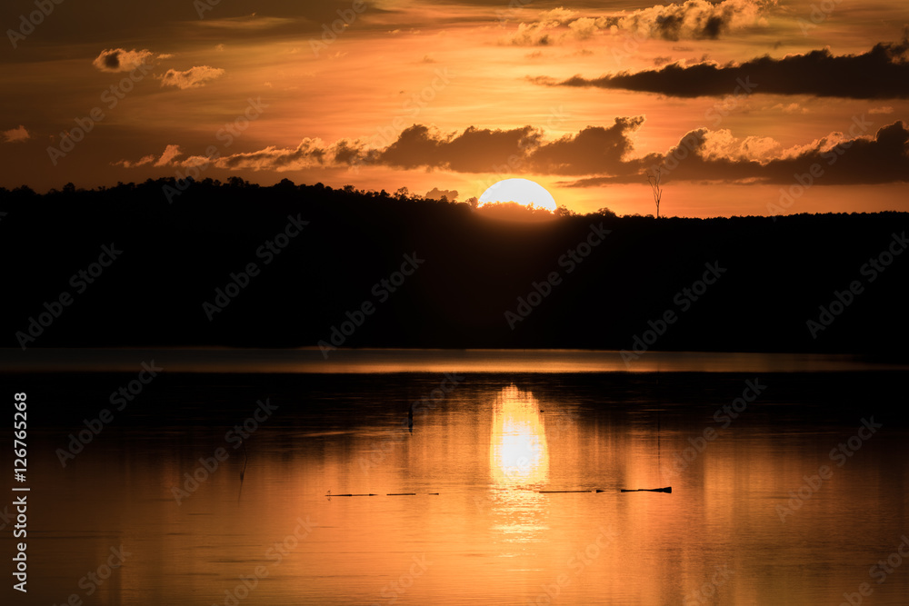 Beautiful orange sky dark clouds at sunset reflection on the lake water with silluette of mountain - Half of a Yellow Sun
