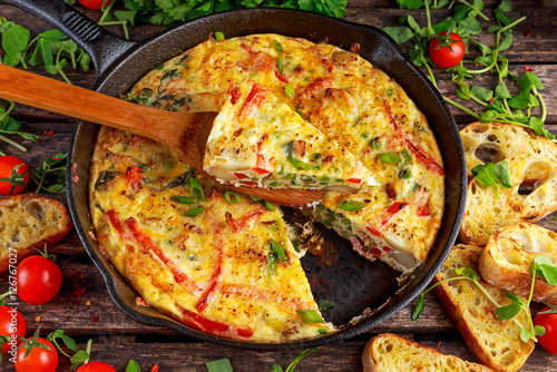 Frittata made of eggs, potato, bacon, paprika, parsley, green peas, onion, cheese in iron pan. on wooden table. photo