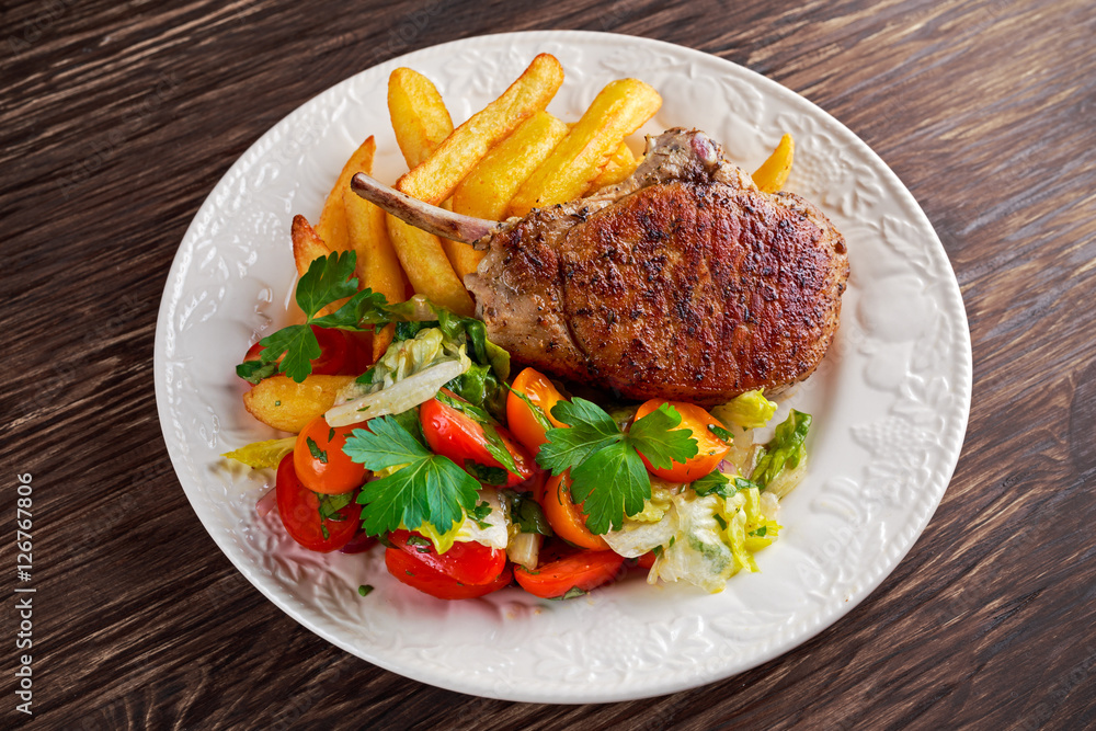 Grilled pork cutlet meat garnished with potato and salad on a wooden table. Grilled pork cutlet meat garnished with potato and salad on a wooden table.