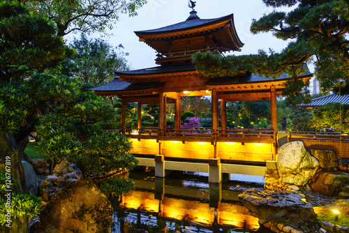 Illuminated wooden pagoda by the pond with trout in Nan Lian Garden at Diamond Hill in Hong Kong twilight scenery