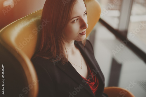 Young business woman in red dress and jacket on armchair