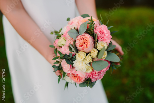 holding a wedding bouquet of pink and white flowers in hands, with a luxurious ring in the tender rich dress, smiling, sensual moment
