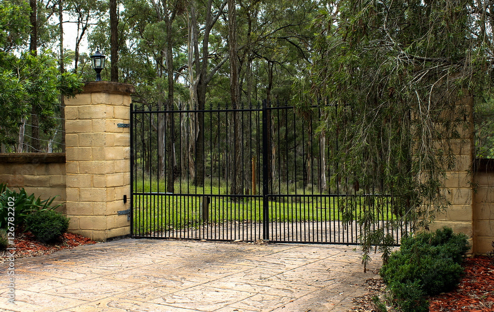 Black metal driveway entrance gates set in brick fence Black metal driveway entrance gates set in brick fence
