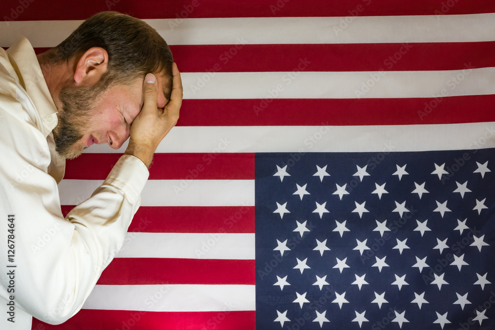 Presidential election disbelief. Man with head in hands in front of an upside down American flag. Protest concept.