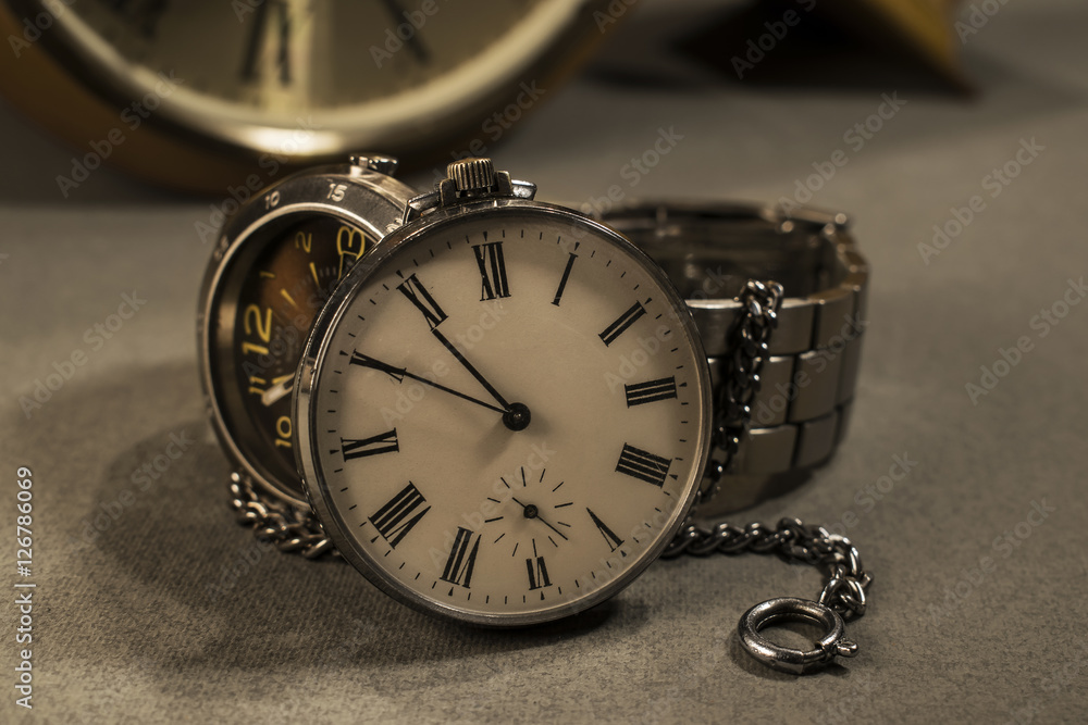 Old pocket watch and modern watch in close-up view with old wall clock in background