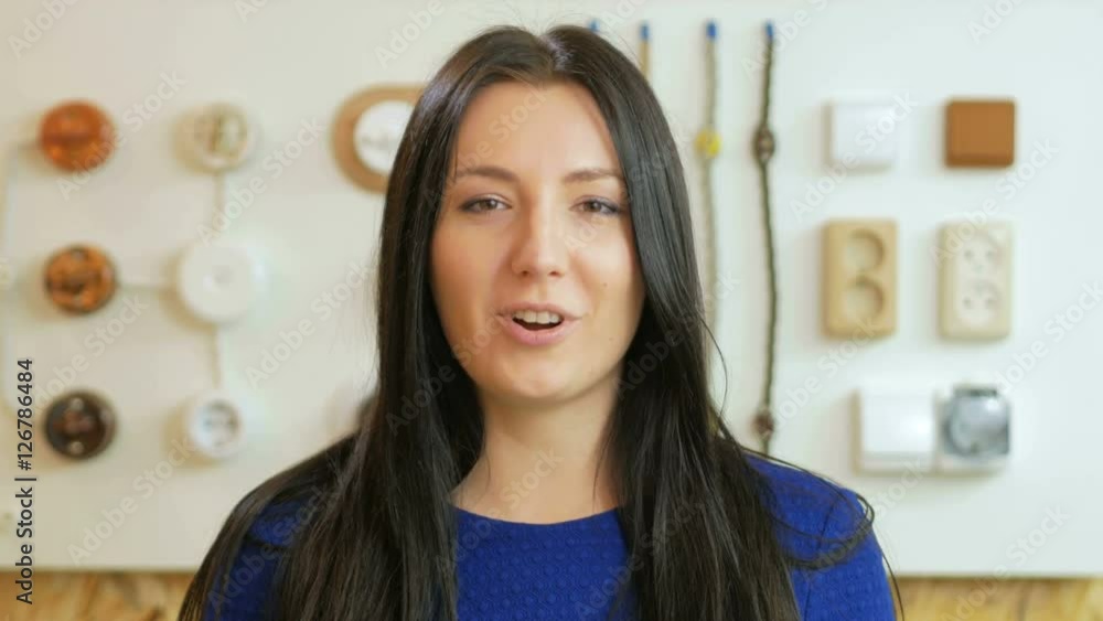 A young woman tells the switch sockets and wires of different colors and shapes. Samples are presented on a special stand on the background. Looking at the camera A young woman tells the switch sockets and wires of different colors and shapes. Samples are presented on a special stand on the background. Looking at the camera