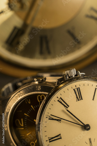 Old pocket watch and modern watch in close-up view with old wall clock in background