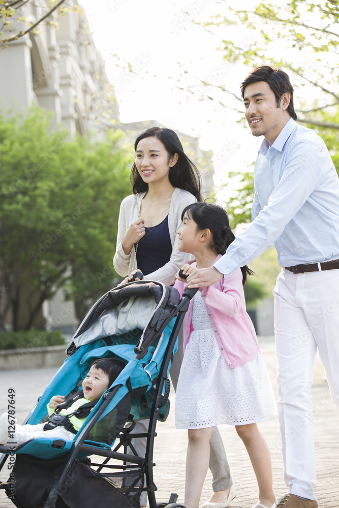 Happy young family taking a walk with baby in pram Happy young family taking a walk with baby in pram