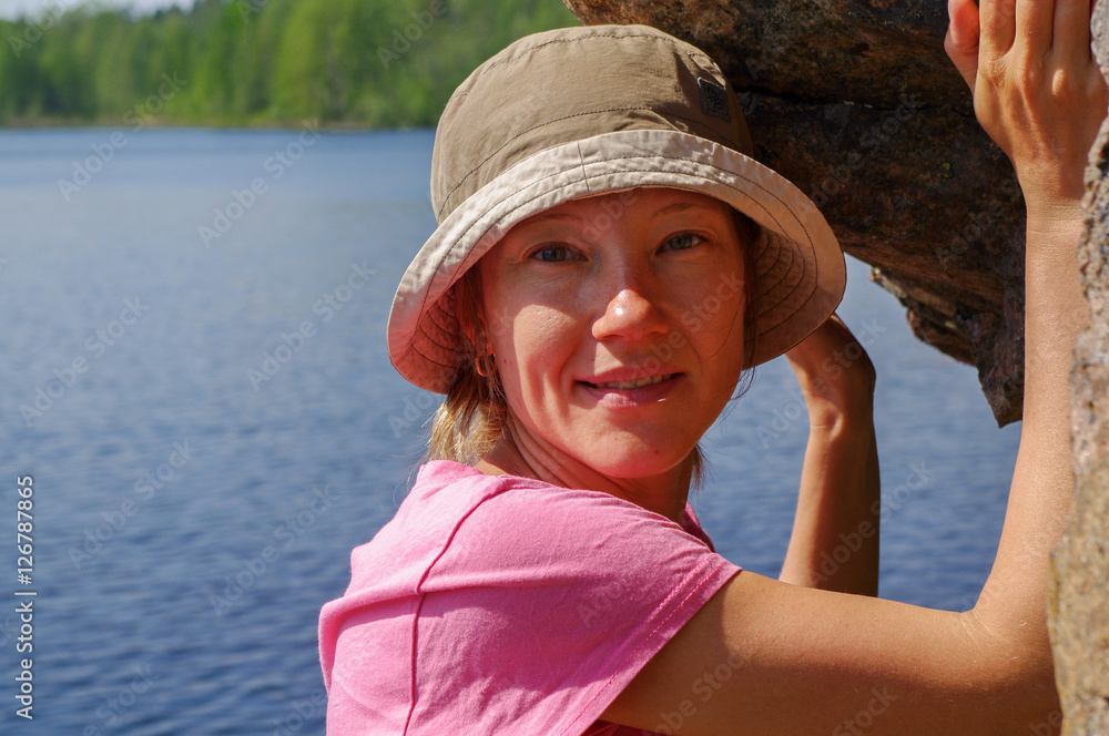 Smiling girl in cap with lake amd water background standing under a rock